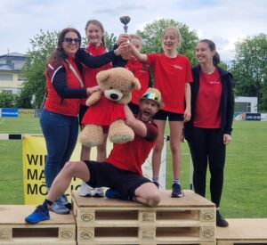 Die Trainer*innen der Leichtathletik Rankweil mit drei Athletinnen, die einen Pokal in der Hand halten.
