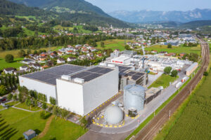 Luftaufnahme des Produktionsstandorts von 11er mit Gebäuden, Biogasanlage, Photovoltaikflächen und umliegender Landschaft bzw. Ortschaften.