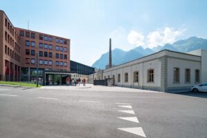 Eingangsbereich des Getzner-Textil-Standorts in Bludenz mit historischem Fabriksgebäude, modernem Zubau und Bergkulisse im Hintergrund.